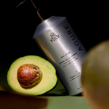 Acure body lotion next to an avocado on a dark background
